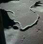 Apollo 15 image of landing site. In image view are a few impact craters, a sinuous or winding channel formed from flowing lava, and the base of two mountains or massifs in the upper right and lower left corners.